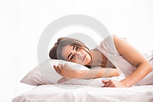 woman is lying in bed with her head on the pillow and hands under it.