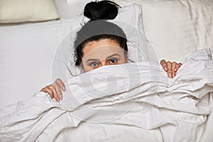 Woman is lying in bed and hiding under blanket
