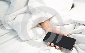 Woman lying on the bed and holding smartphone in hand, Social Addict Concept. Woman sleeping in bed being woken by mobile phone