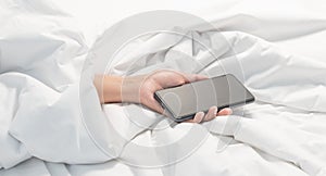 Woman lying on the bed and holding smartphone in hand, Social Addict Concept. Woman sleeping in bed being woken by mobile phone
