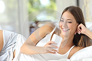 Woman lying on a bed at home using a smart phone