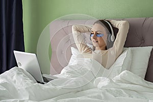 Woman lying in bed listening to music, audiobook, podcast, enjoying meditation for sleep and peace of mind in wireless