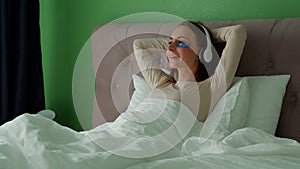 Woman lying in bed listening to music, audiobook, podcast, enjoying meditation for sleep and peace of mind in wireless