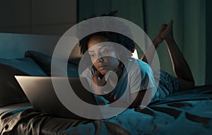 Woman lying in bed at night and connecting with her laptop