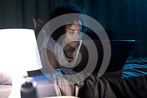 Woman lying in bed at night and connecting with her laptop