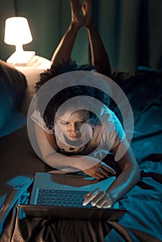 Woman lying in bed at night and connecting with her laptop