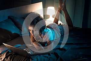 Woman lying in bed at night and connecting with her laptop