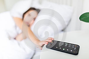 Young Woman Lying on Bed Snoozing Alarm On Mobile Phone photo