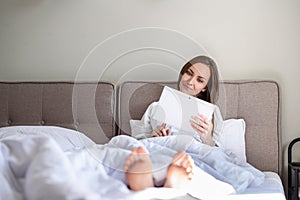 Woman lying in bed under blanket in tablet, Internet surfing, news, good morning