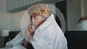 A woman lying on a bed uses a drop in her nose to treat a cold as prescribed by a doctor