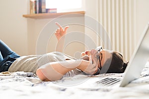 Woman lying on bed, working on laptop, calling. Home office.