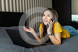 Woman lying on bed, working on laptop, calling. Home office