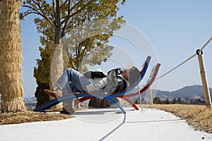 A woman is lying on a bench and shading her face with her hands