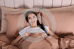 Woman lying in comfortable bed with beige linens, above view