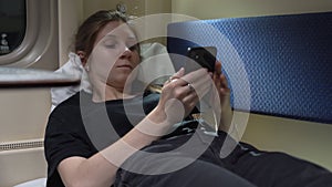 Woman is lying in a compartment car near the window with a phone in her hand and surfing messengers