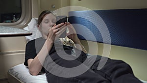 Woman is lying in a compartment car near the window with a phone in her hand and surfing messengers