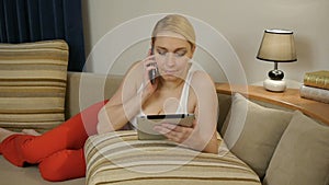 Woman lying on the couch with a computer tablet and talking on the phone
