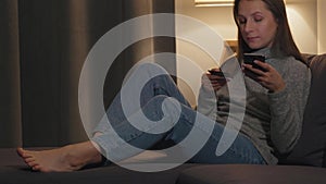 Woman lying on the couch in a cozy room and makes an online purchase using a credit card and your smartphone. Online