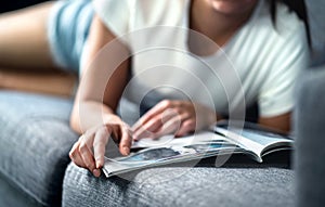 Woman lying on couch and reading a fashion or beauty magazine. Lady enjoying her day off with celebrity entertainment news.