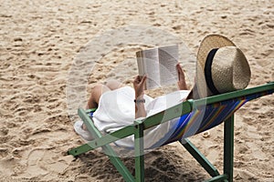 Woman lying down and reading book on the beach chair with feeling relaxed