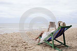 A woman lying down and reading book on the beach chair with feeling relaxed