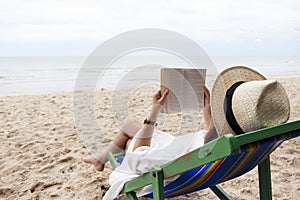 A woman lying down and reading book on the beach chair with feeling relaxed