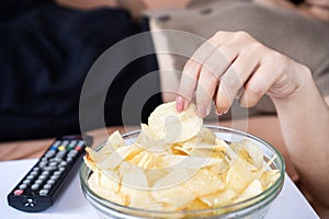 woman lying down on sofa eating potato chips, unhealthy eating lifestyle photo