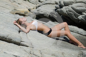 Woman is lying down and sunbathing on solid rocks