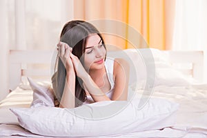 A woman lying at the end of the bed underneath the quilt and smiling, with her head resting upon her hand