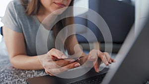 Woman is lying on the floor and and makes an online purchase using a credit card and laptop. Online shopping, lifestyle