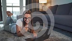 Woman is lying on the floor and and makes an online purchase using a credit card and laptop. Online shopping, lifestyle