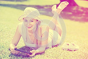 Woman lying on green grass in park and holding mobile phone in h