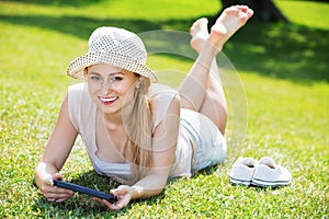 Woman lying on green grass in park and holding mobile phone in h