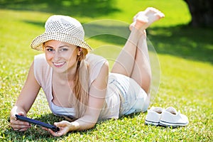 Woman lying on green grass in park and holding mobile phone in hands