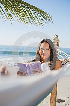 Woman lying on hammock holding book and smiling at camera