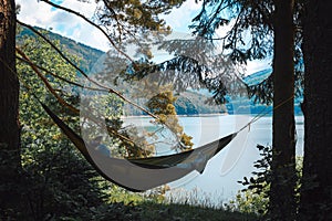 Woman lying on hammock near tent on green meadow near lake. Girl wear sportswear. Concept of resting and tourism on nature.
