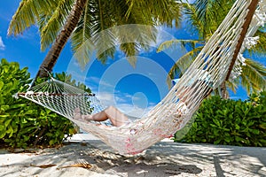 Woman lying on hammock between palms on a tropical beach. Maldives