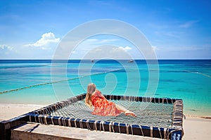 Woman lying on hammock on tropical beach, enjoying turquoise water and blue sky