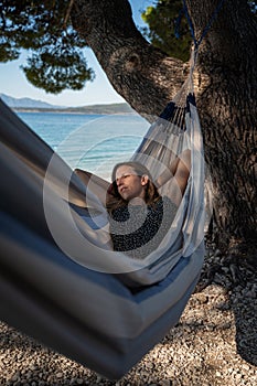 Woman lying in a hammock under a pine tree by the sea