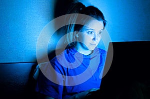 Woman lying with her laptop in night in the bedroom in blue light at screen