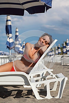 Woman lying on lounger under beach umbrella