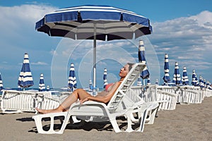 Woman lying on lounger under beach umbrella