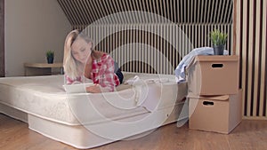 Woman lying on the mattress in her new flat and using on tablet.