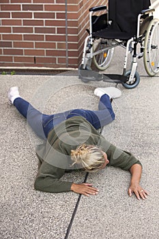 Woman lying on pavement next to wheelchair