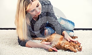 A woman is lying with a red cat on the carpet and petting her pet