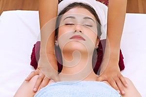 Woman lying on red towel while receiving massage in spa salon with masseuse hands. Relax girl getting treatment on her body