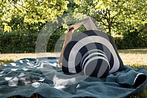 Woman lying on a rug in the shade of a tree reading a book