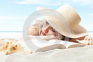 woman lying on sand beach with book, resting wear sun straw hat for sun protection her skin face. Concept of summer beach holiday