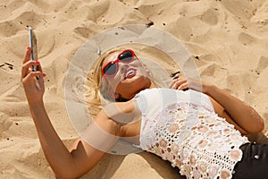 Woman lying on sandy beach using cell phone