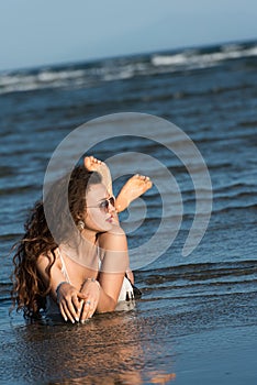 Woman lying in sea water wear bikini, sunglasses and white shirt